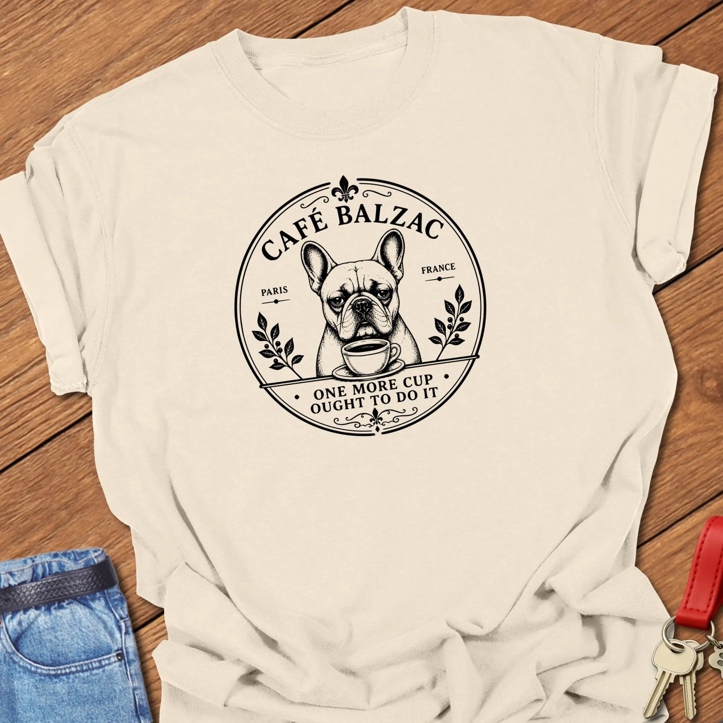 Café Balzac French Bulldog graphic t-shirt featuring "One More Cup Ought To Do It" slogan with vintage Paris café artwork inspired by literary coffee culture in Ivory color.