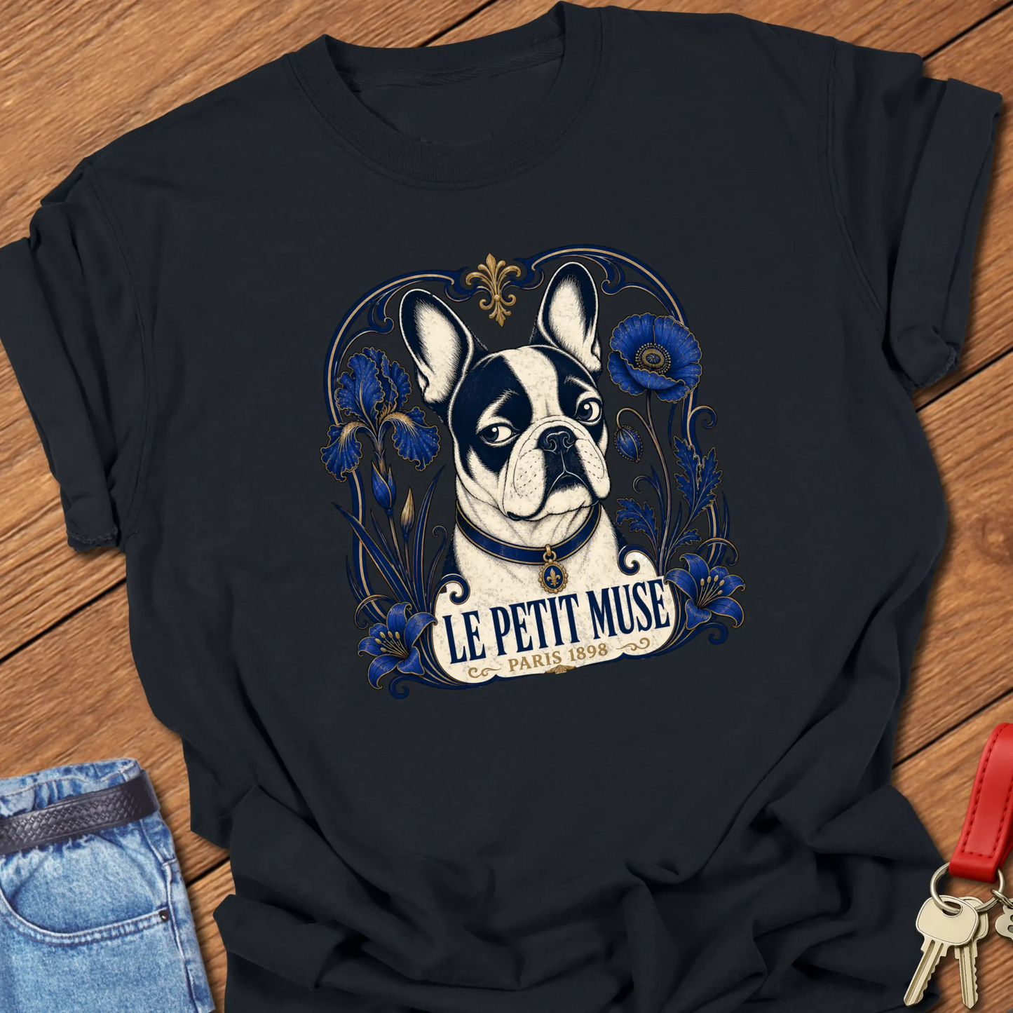 Art Nouveau-inspired French Bulldog portrait surrounded by cobalt-blue floral ornamentation with the title "Le Petit Muse — Paris 1898" printed on a Comfort Colors® garment-dyed t-shirt in Black color.
