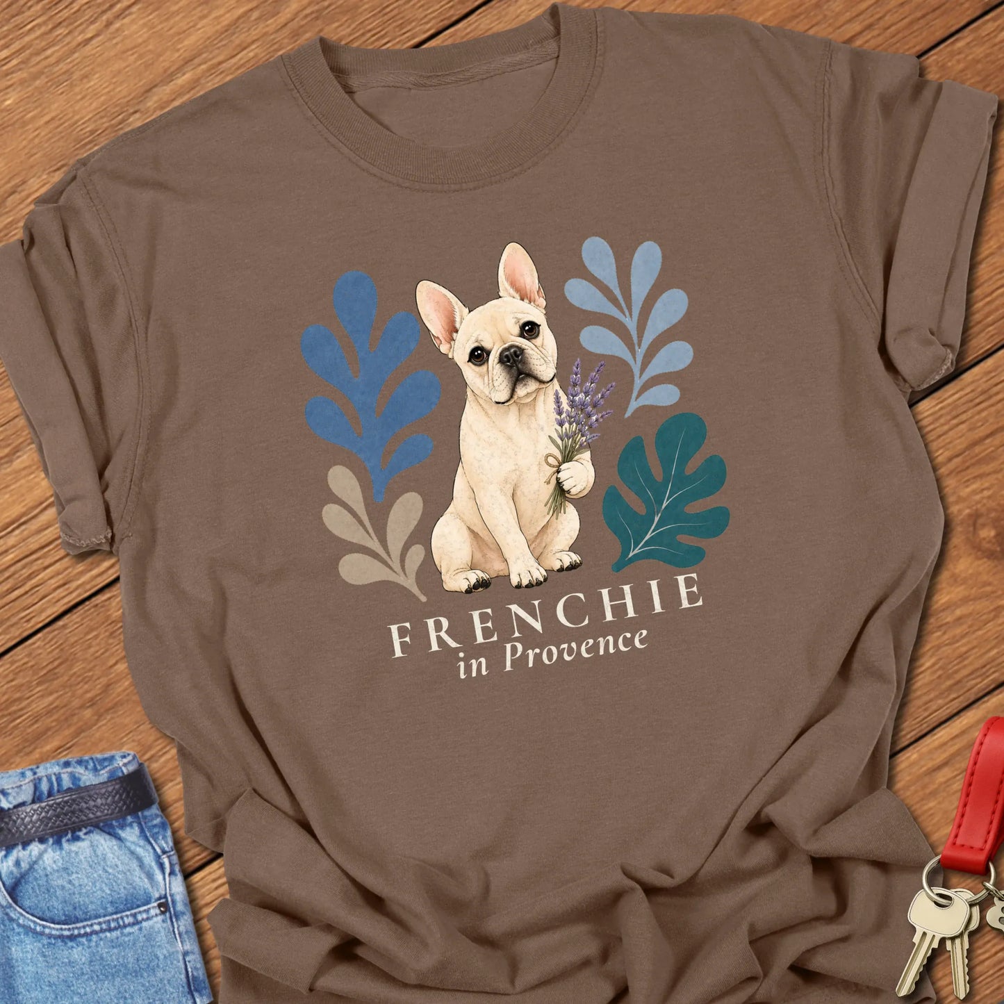 Cream French Bulldog holding a lavender bouquet surrounded by botanical artwork with the phrase "Frenchie in Provence" printed on a Comfort Colors® garment-dyed t-shirt in Espresso color.