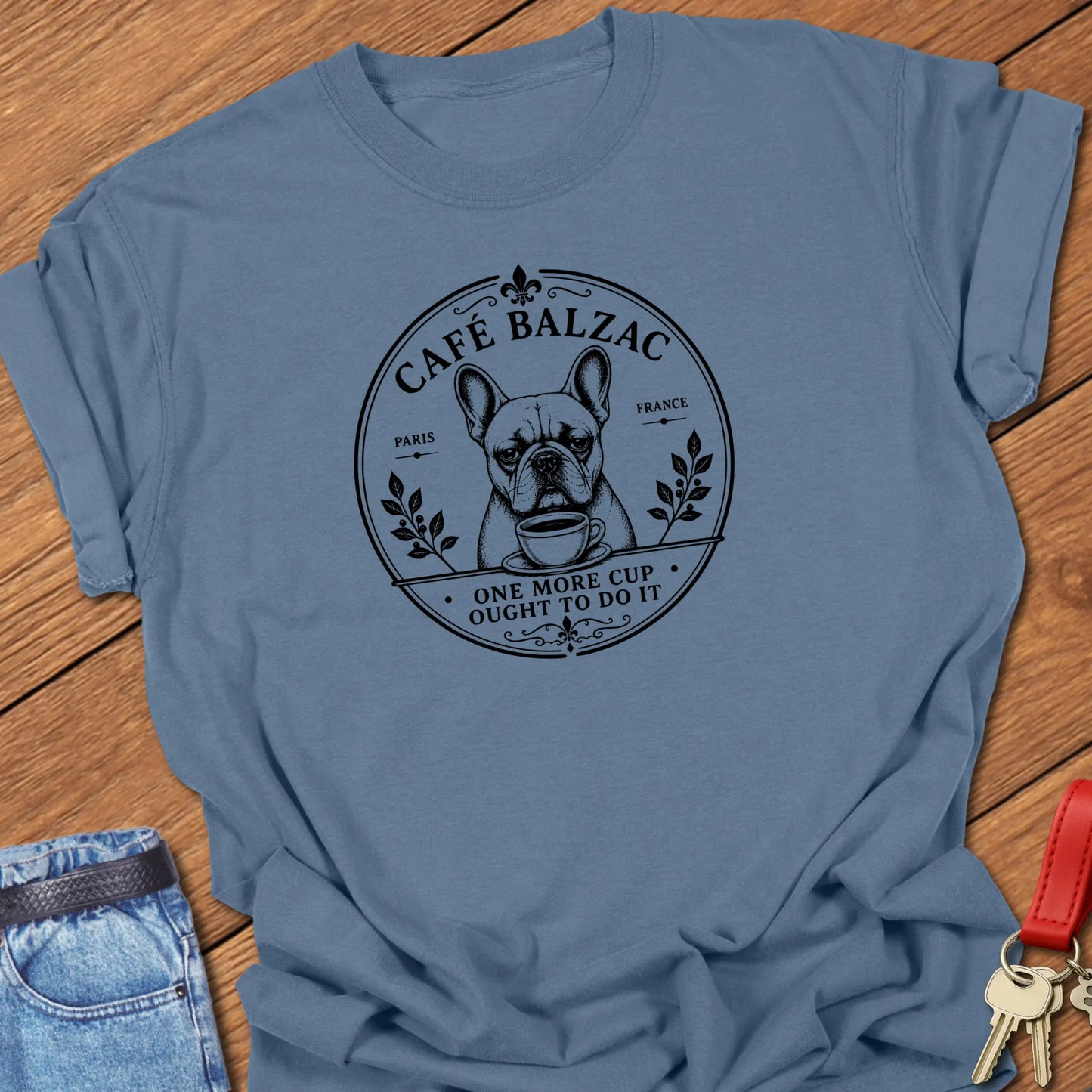 Café Balzac French Bulldog graphic t-shirt featuring "One More Cup Ought To Do It" slogan with vintage Paris café artwork inspired by literary coffee culture in Blue Jean color.