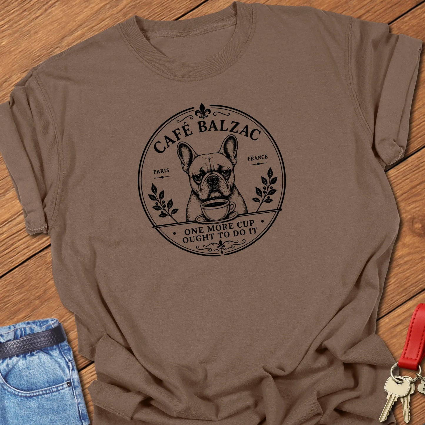 Café Balzac French Bulldog graphic t-shirt featuring "One More Cup Ought To Do It" slogan with vintage Paris café artwork inspired by literary coffee culture in Espresso color.