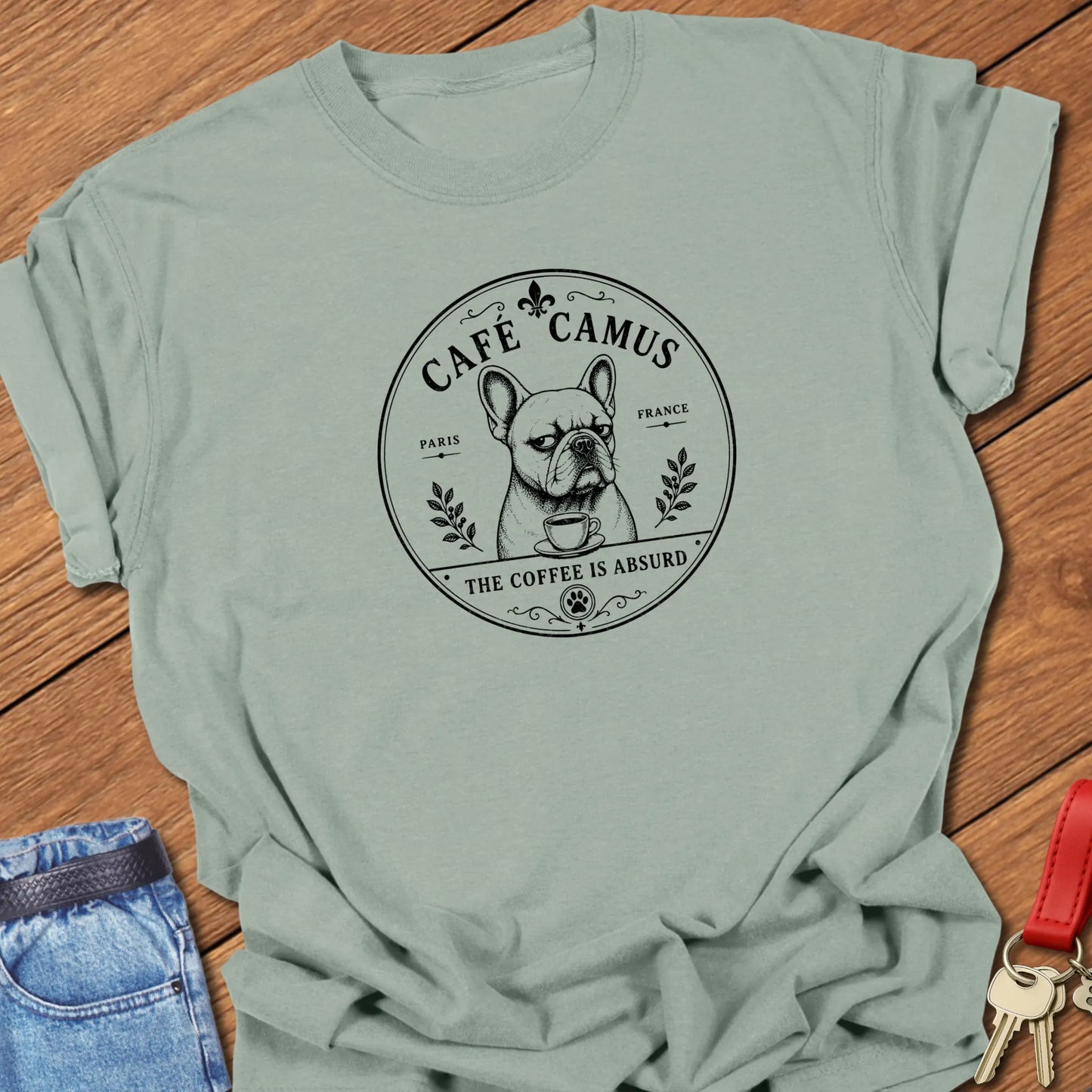 Café Camus French Bulldog literary coffee t-shirt featuring the slogan "The Coffee Is Absurd" in Bay color with vintage Paris café-inspired artwork.