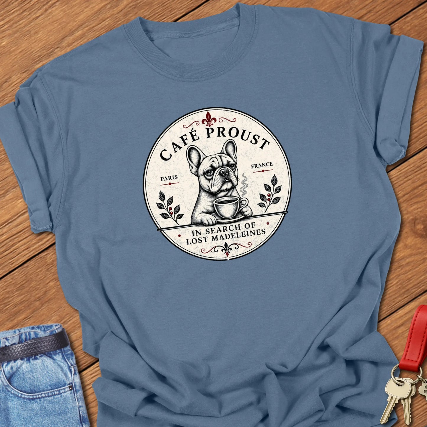 Café Proust French Bulldog graphic t-shirt featuring the phrase "In Search of Lost Madeleines" with vintage Paris café artwork in Blue Jean color.
