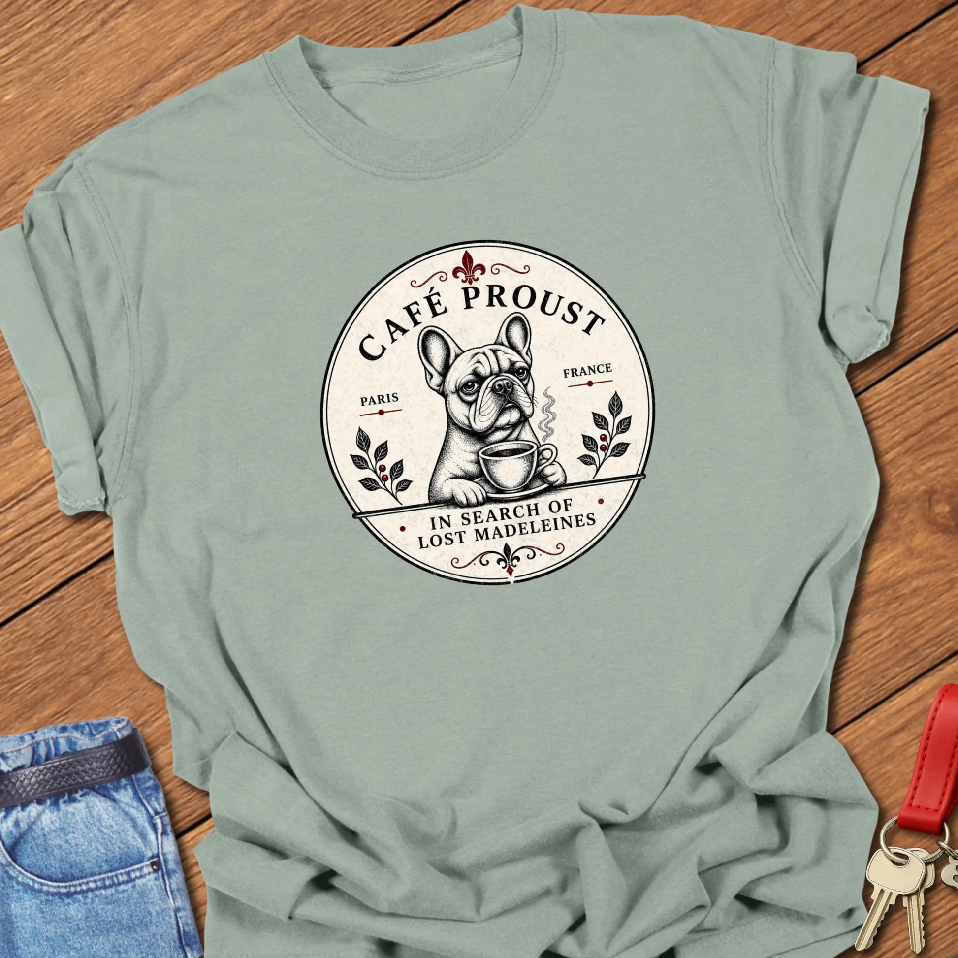 Café Proust French Bulldog graphic t-shirt featuring the phrase "In Search of Lost Madeleines" with vintage Paris café artwork in Bay color.