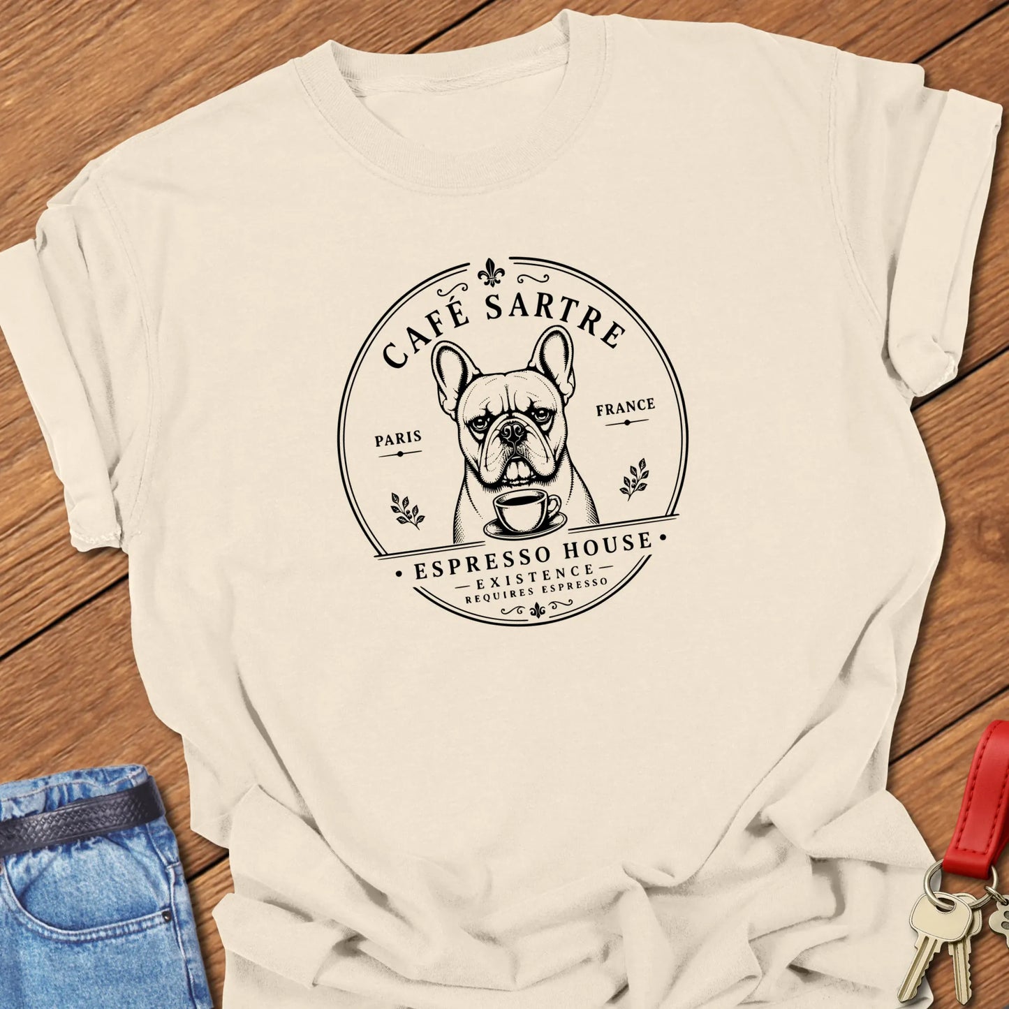 Café Sartre French Bulldog graphic t-shirt featuring "Existence Requires Espresso" slogan with vintage Paris café artwork in Ivory color.