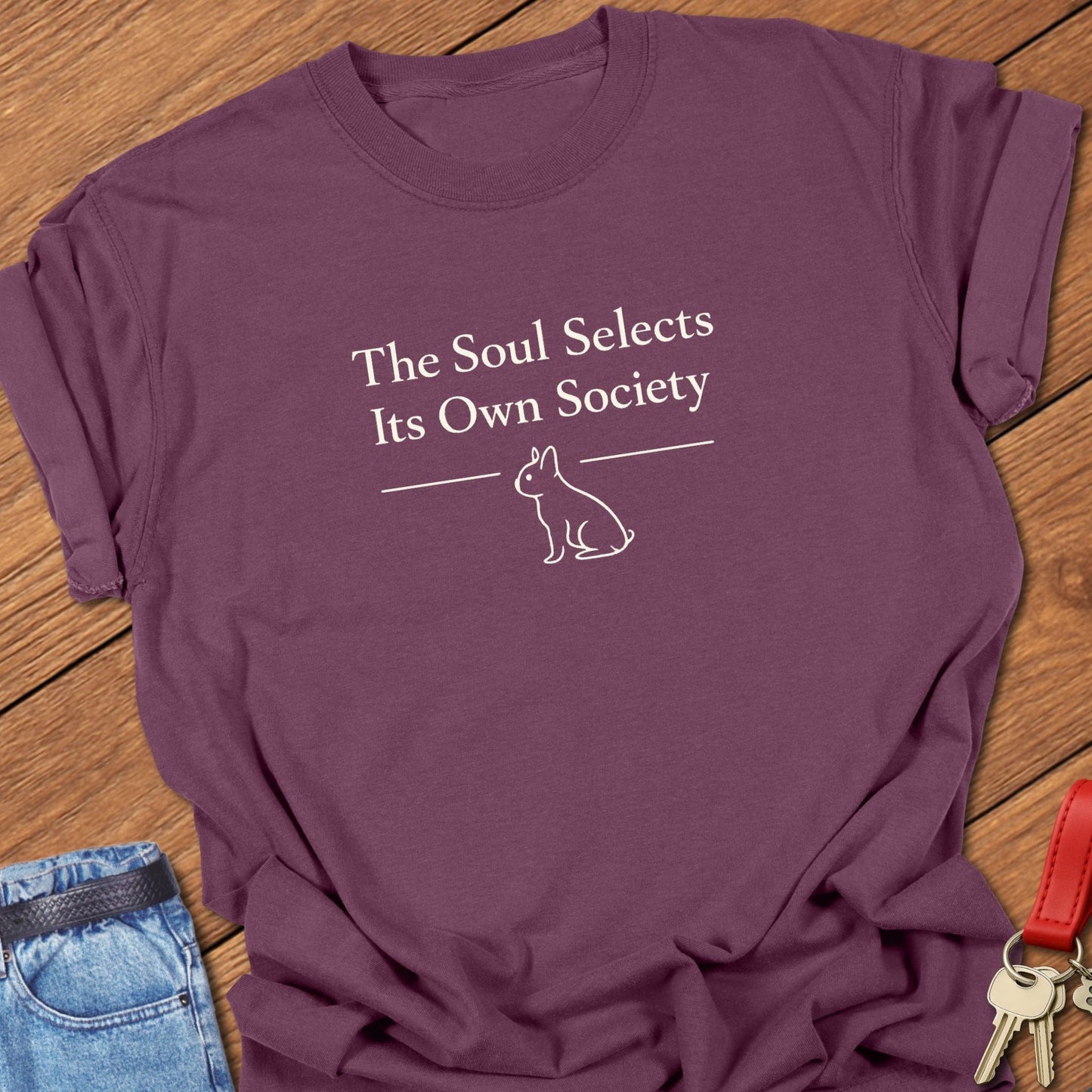 Ivory serif text reading “The Soul Selects Its Own Society” by Emily Dickinson above a minimalist French bulldog silhouette printed on a Comfort Colors berry t shirt.