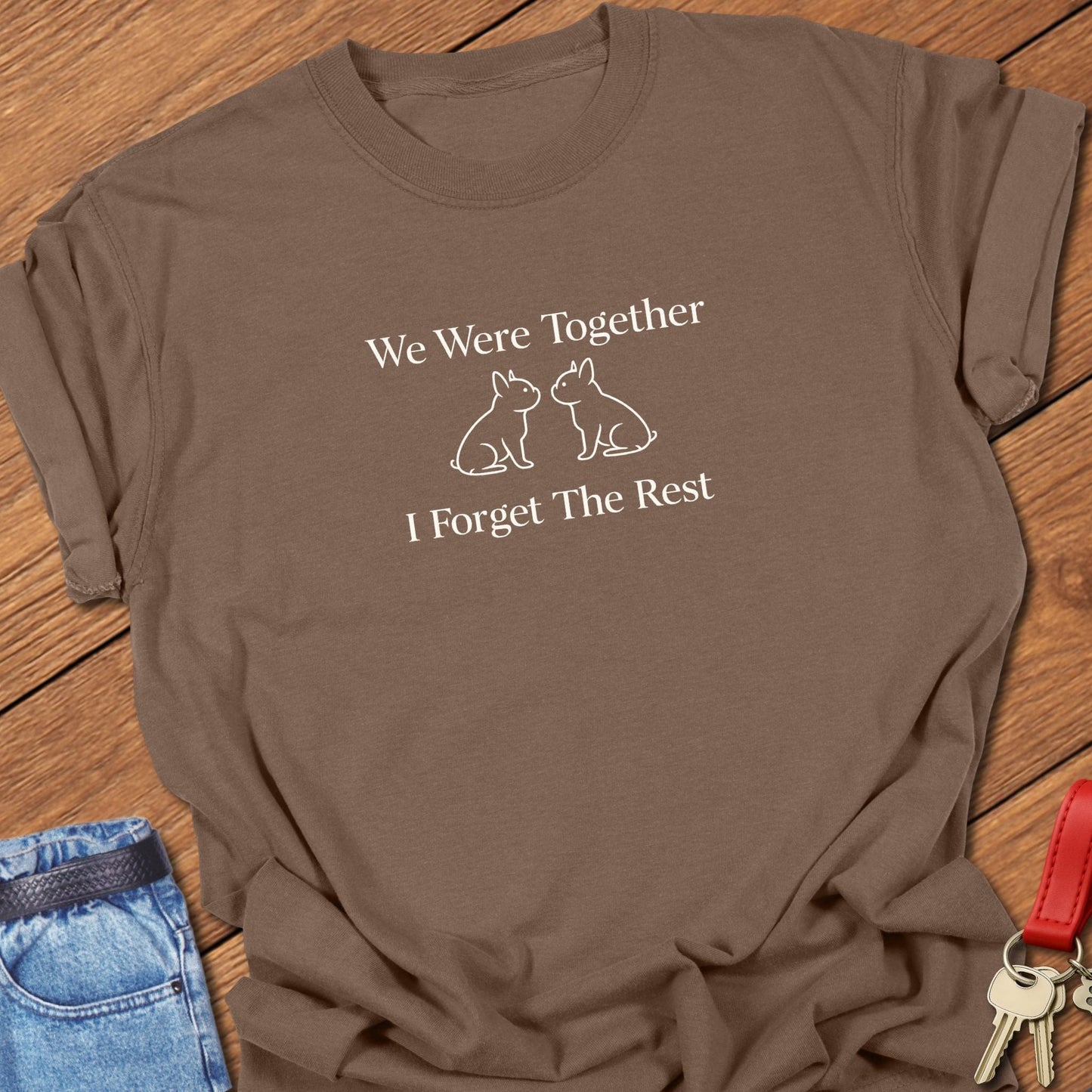 Ivory serif text reading “We Were Together I Forget The Rest” inspired by Walt Whitman, with two minimalist French bulldog silhouettes printed on a espresso Comfort Colors t shirt.