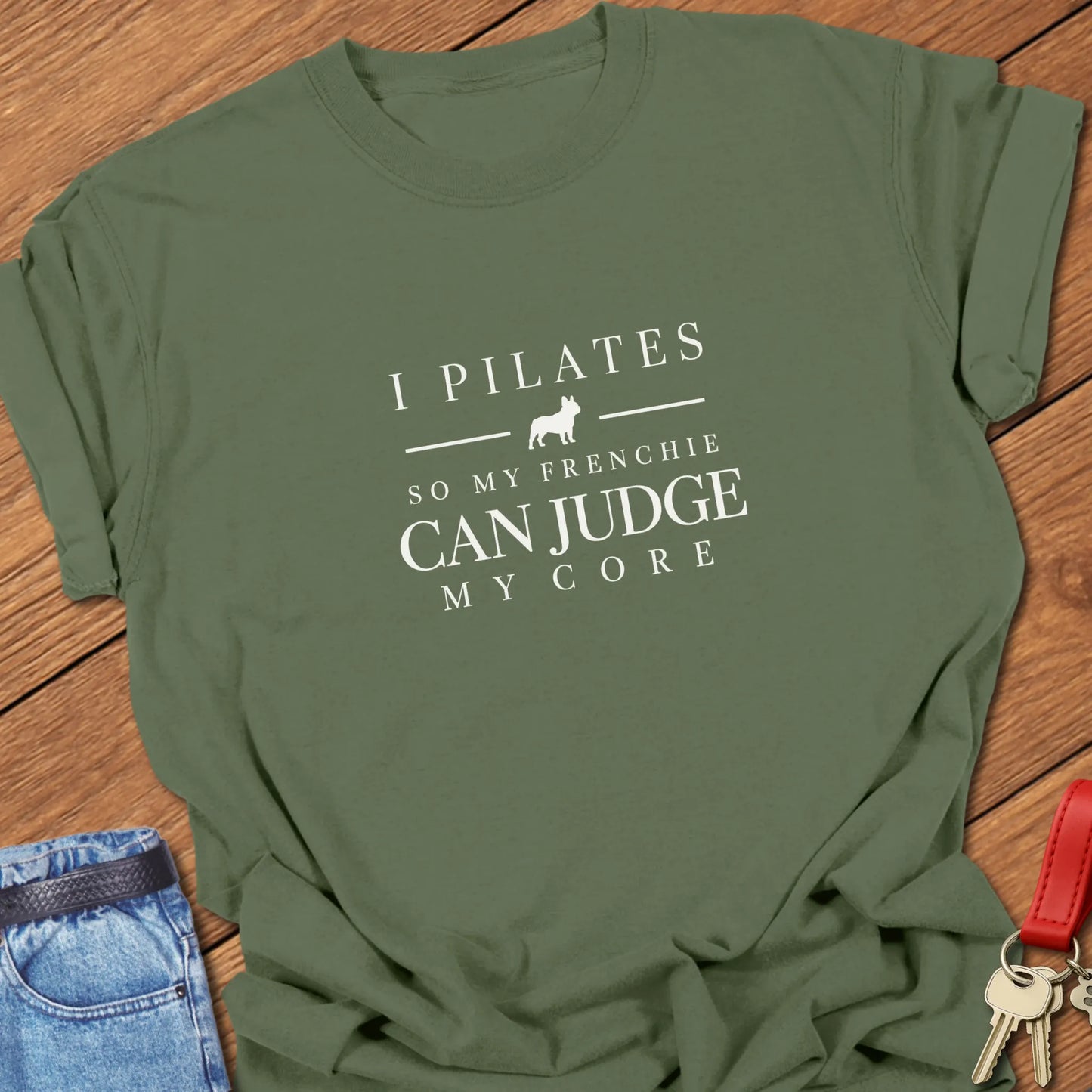 I Pilates So My Frenchie Can Judge My Core slogan featuring a French Bulldog silhouette. On a Comfort Colors 1717 cotton shirt in Moss color.