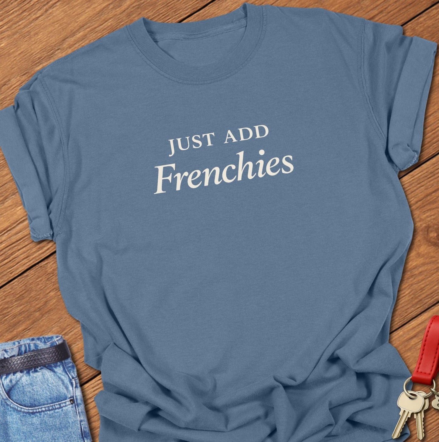 Stacked black serif text reading “JUST ADD Frenchies” printed on a Comfort Colors blue jean t shirt.
