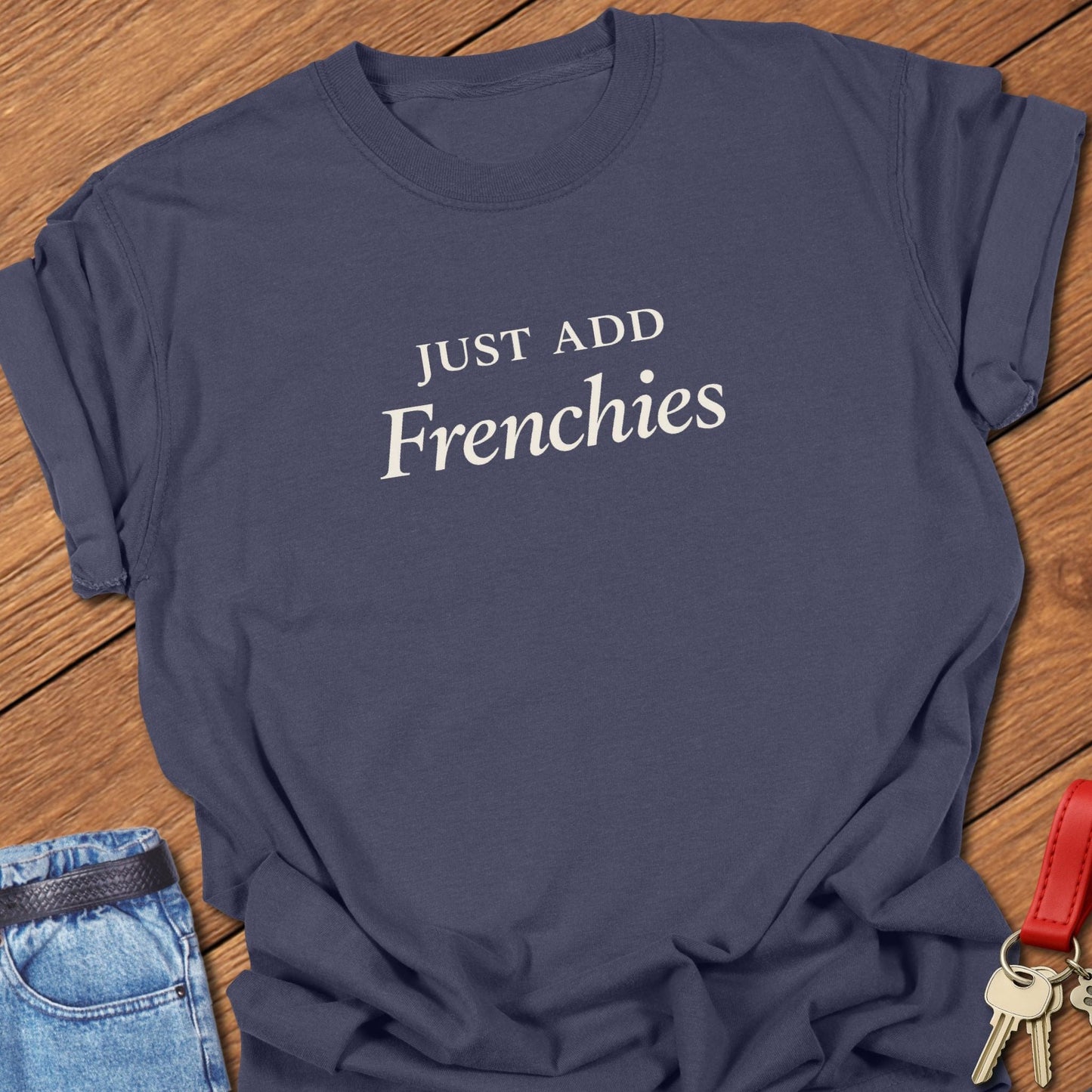 Stacked black serif text reading “JUST ADD Frenchies” printed on a Comfort Colors navy t shirt.