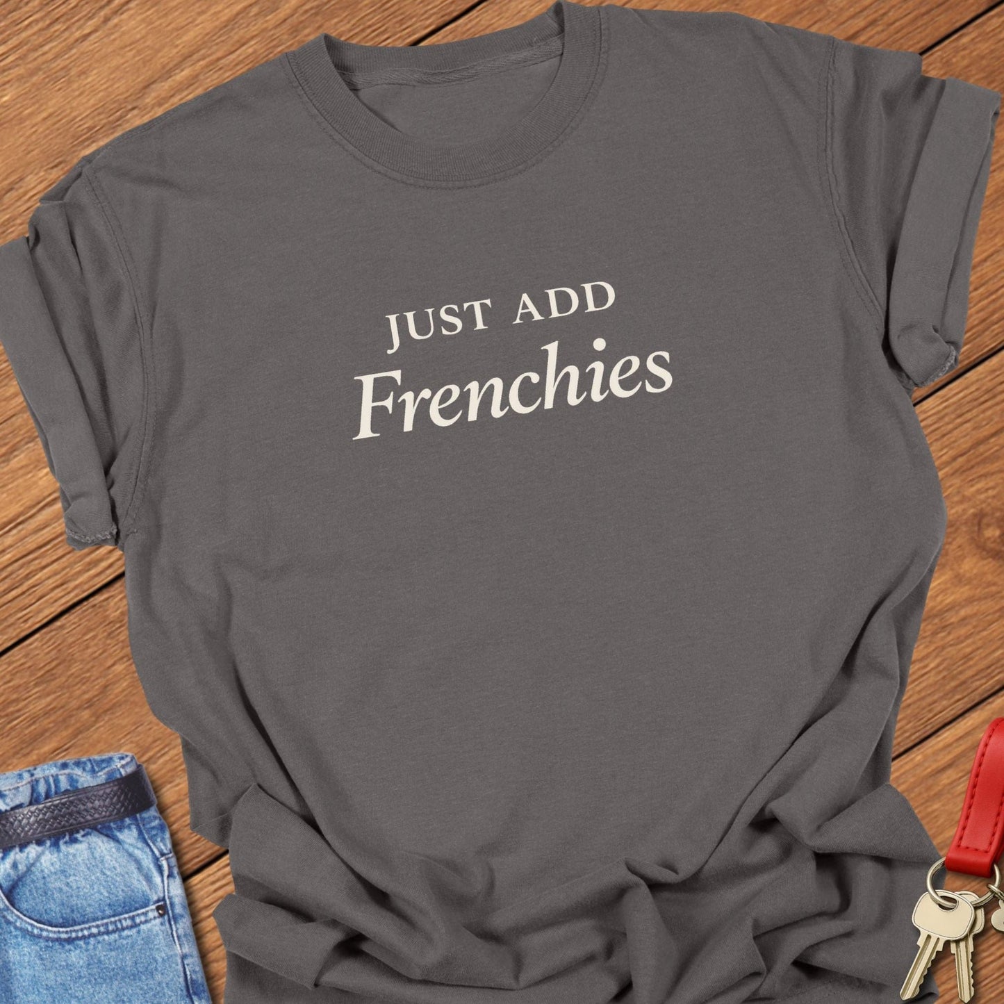 Stacked black serif text reading “JUST ADD Frenchies” printed on a Comfort Colors pepper t shirt.