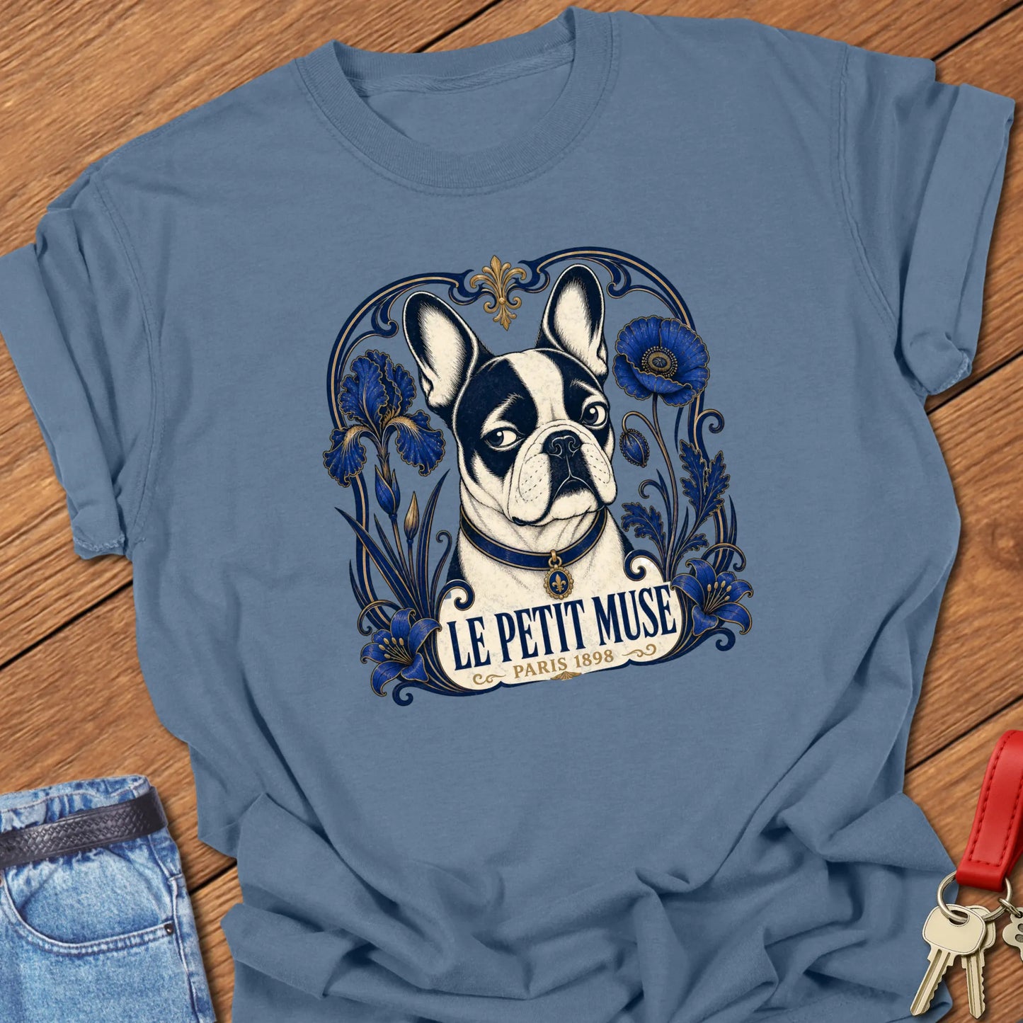 Art Nouveau-inspired French Bulldog portrait surrounded by cobalt-blue floral ornamentation with the title "Le Petit Muse — Paris 1898" printed on a Comfort Colors® garment-dyed t-shirt in Blue Jean color.