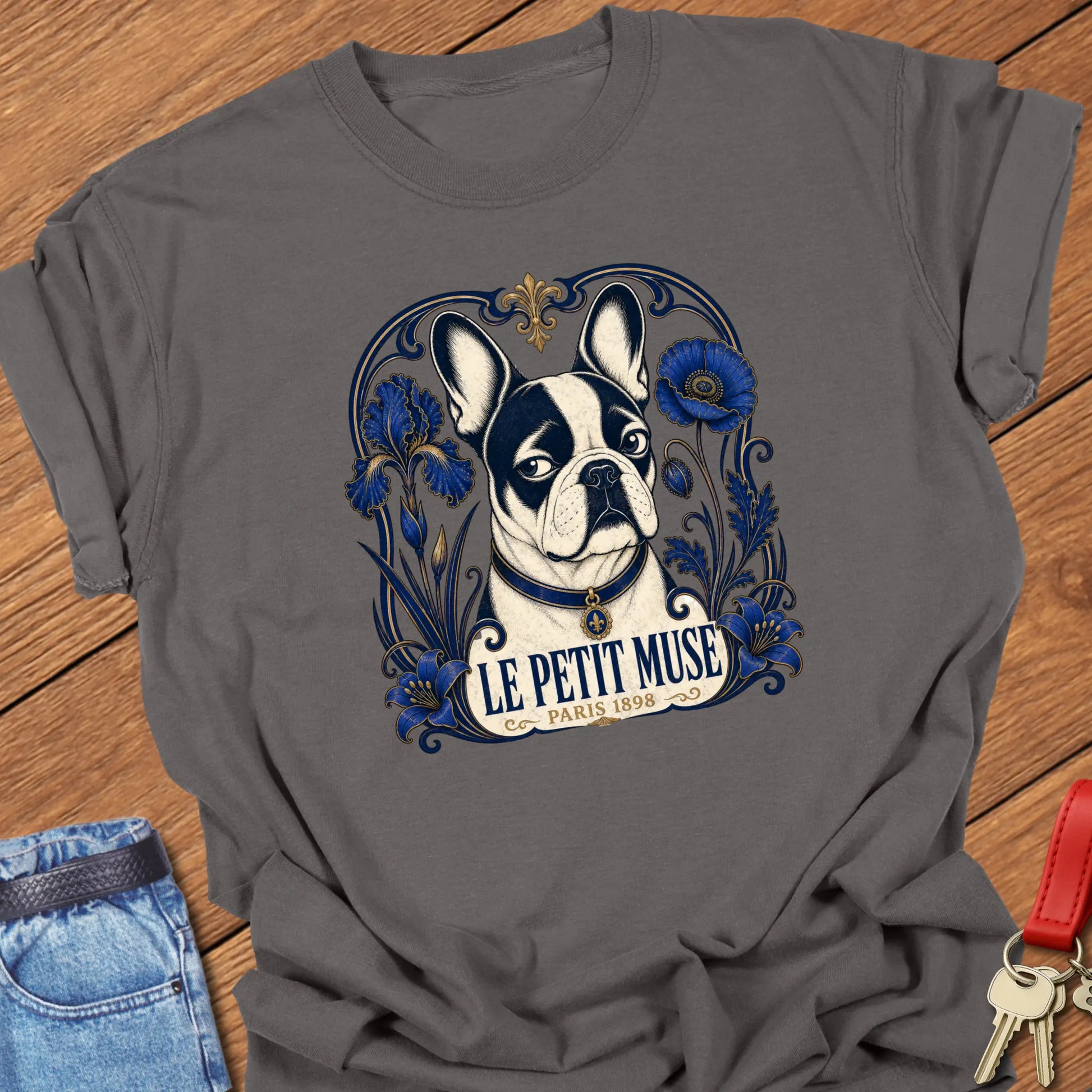 Art Nouveau-inspired French Bulldog portrait surrounded by cobalt-blue floral ornamentation with the title "Le Petit Muse — Paris 1898" printed on a Comfort Colors® garment-dyed t-shirt in Pepper color.
