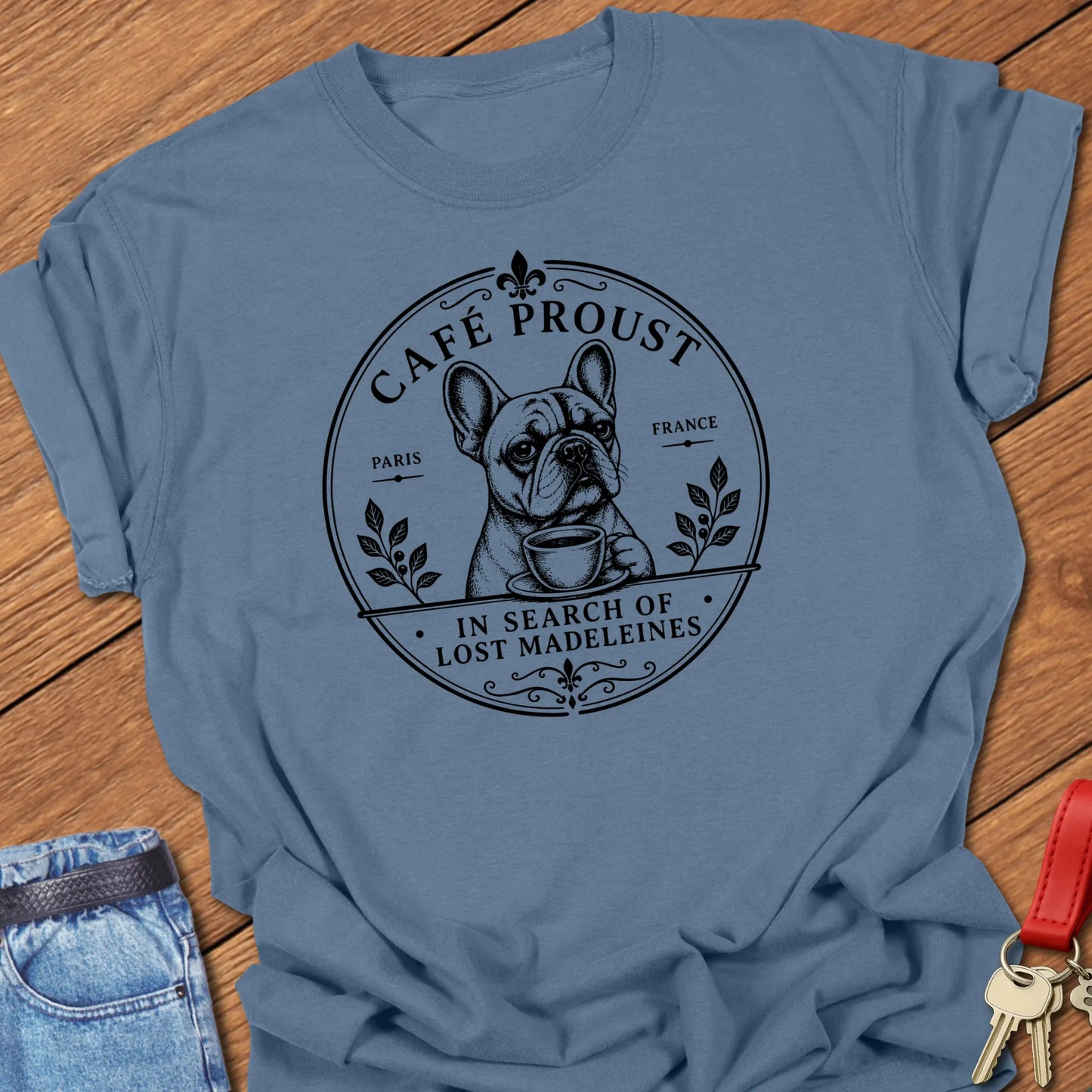 Lost Madeleines French Bulldog graphic t-shirt featuring "In Search of Lost Madeleines" literary café artwork with a thoughtful Frenchie holding a coffee cup in Blue Jean color.