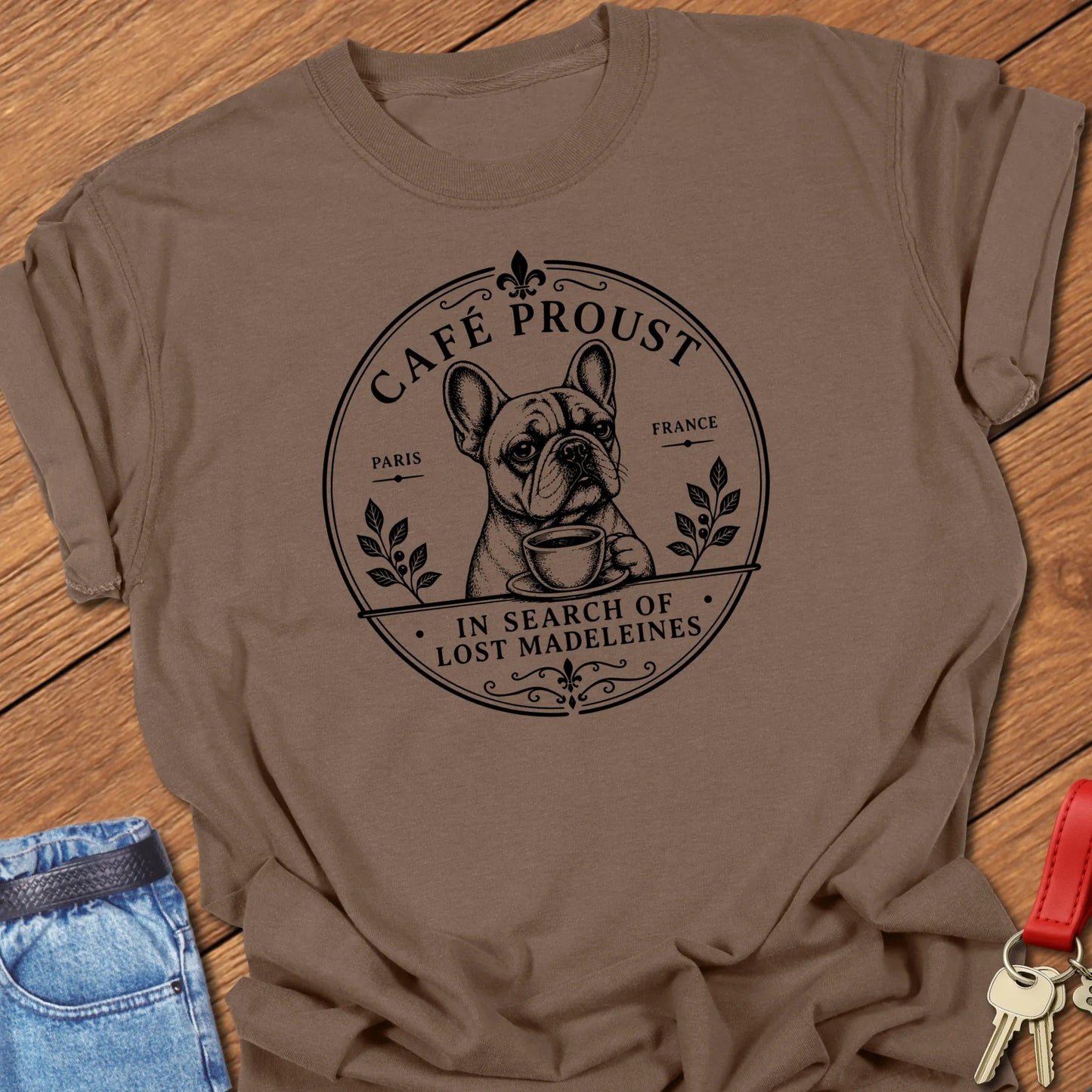 Lost Madeleines French Bulldog graphic t-shirt featuring "In Search of Lost Madeleines" literary café artwork with a thoughtful Frenchie holding a coffee cup in Espresso color.