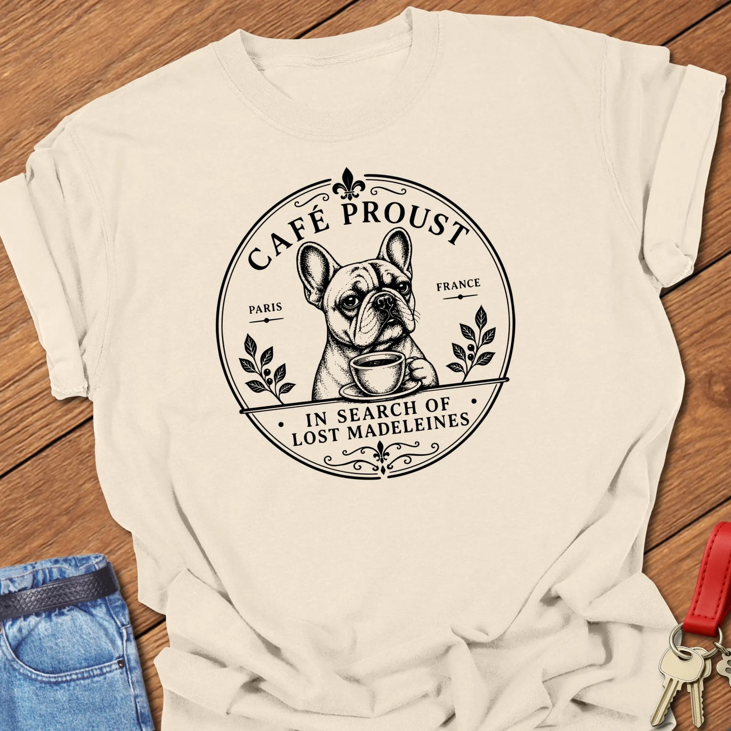 Lost Madeleines French Bulldog graphic t-shirt featuring "In Search of Lost Madeleines" literary café artwork with a thoughtful Frenchie holding a coffee cup in Ivory color.