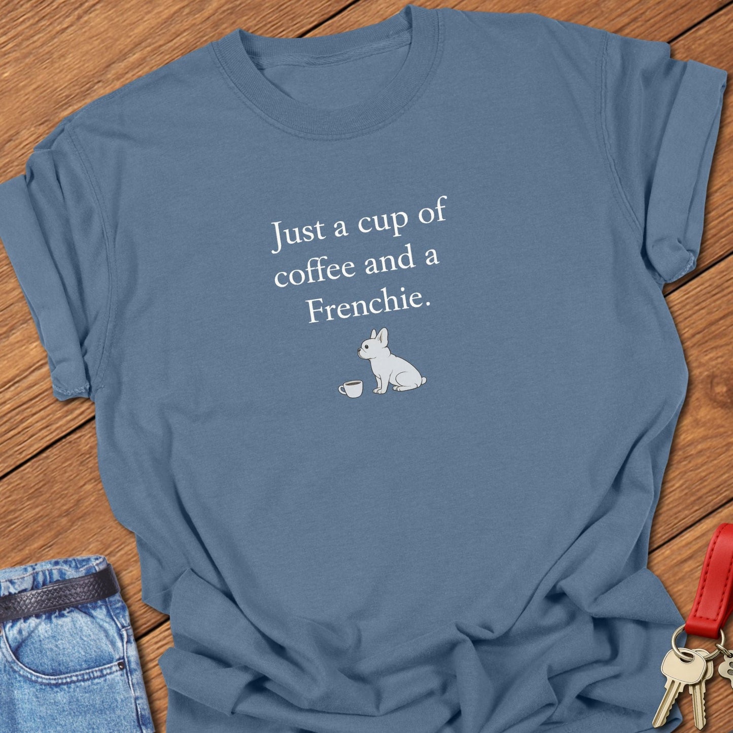 French bulldog sitting beside a coffee cup with text reading “Just a cup of coffee and a Frenchie” on a minimalist graphic T-shirt in blue jean.

