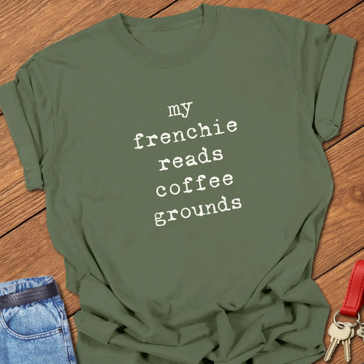 Typewriter-style typography featuring the slogan "My Frenchie Reads Coffee Grounds" printed on a Comfort Colors® garment-dyed t-shirt in Moss color.