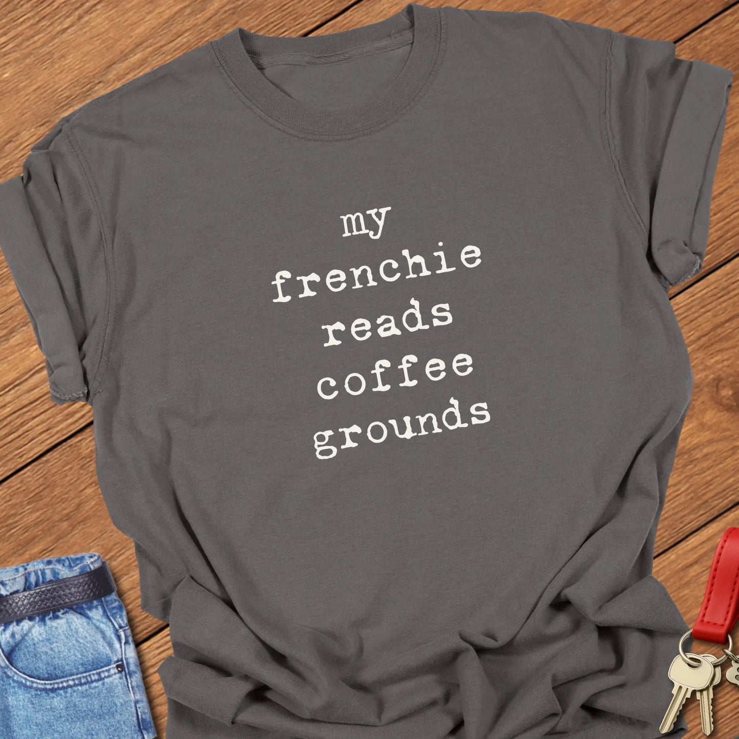 Typewriter-style typography featuring the slogan "My Frenchie Reads Coffee Grounds" printed on a Comfort Colors® garment-dyed t-shirt in Pepper color.