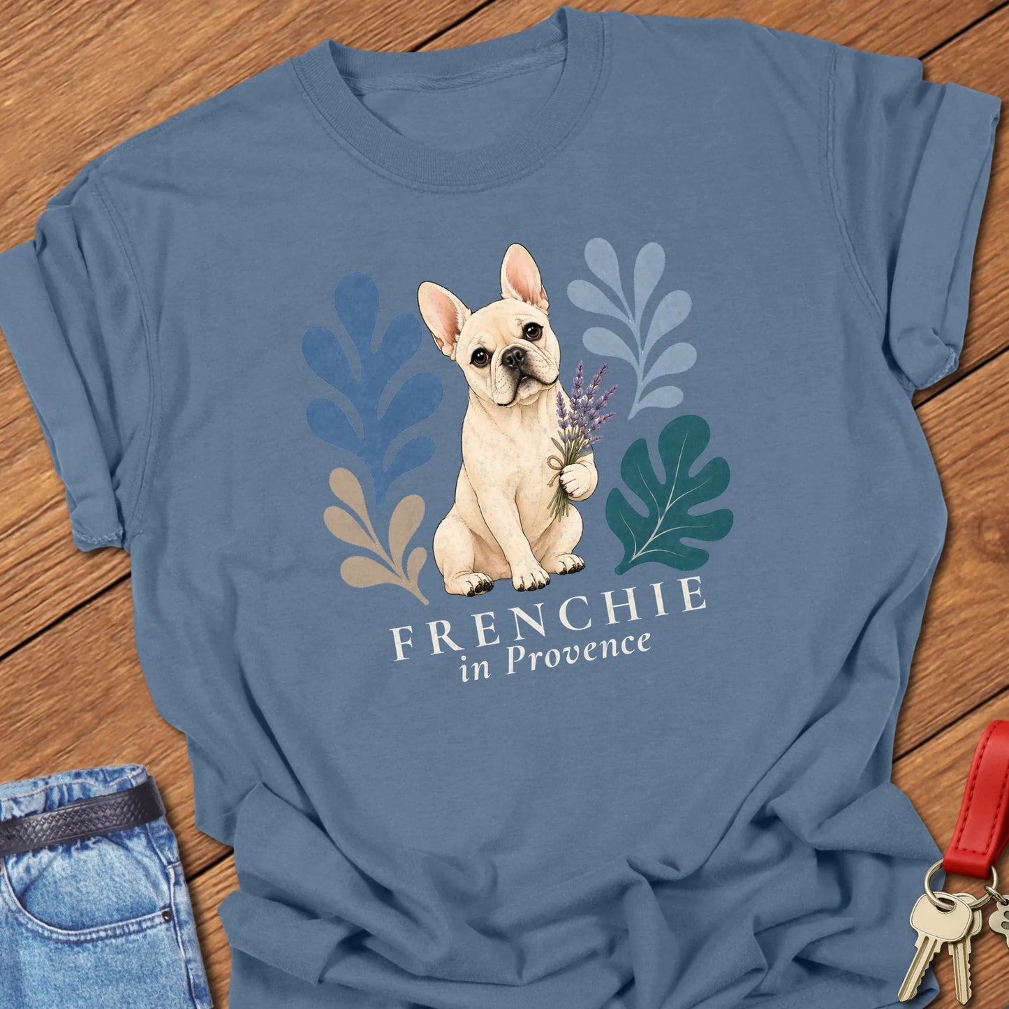 Cream French Bulldog holding a lavender bouquet surrounded by botanical artwork with the phrase "Frenchie in Provence" printed on a Comfort Colors® garment-dyed t-shirt in Blue Jean color.