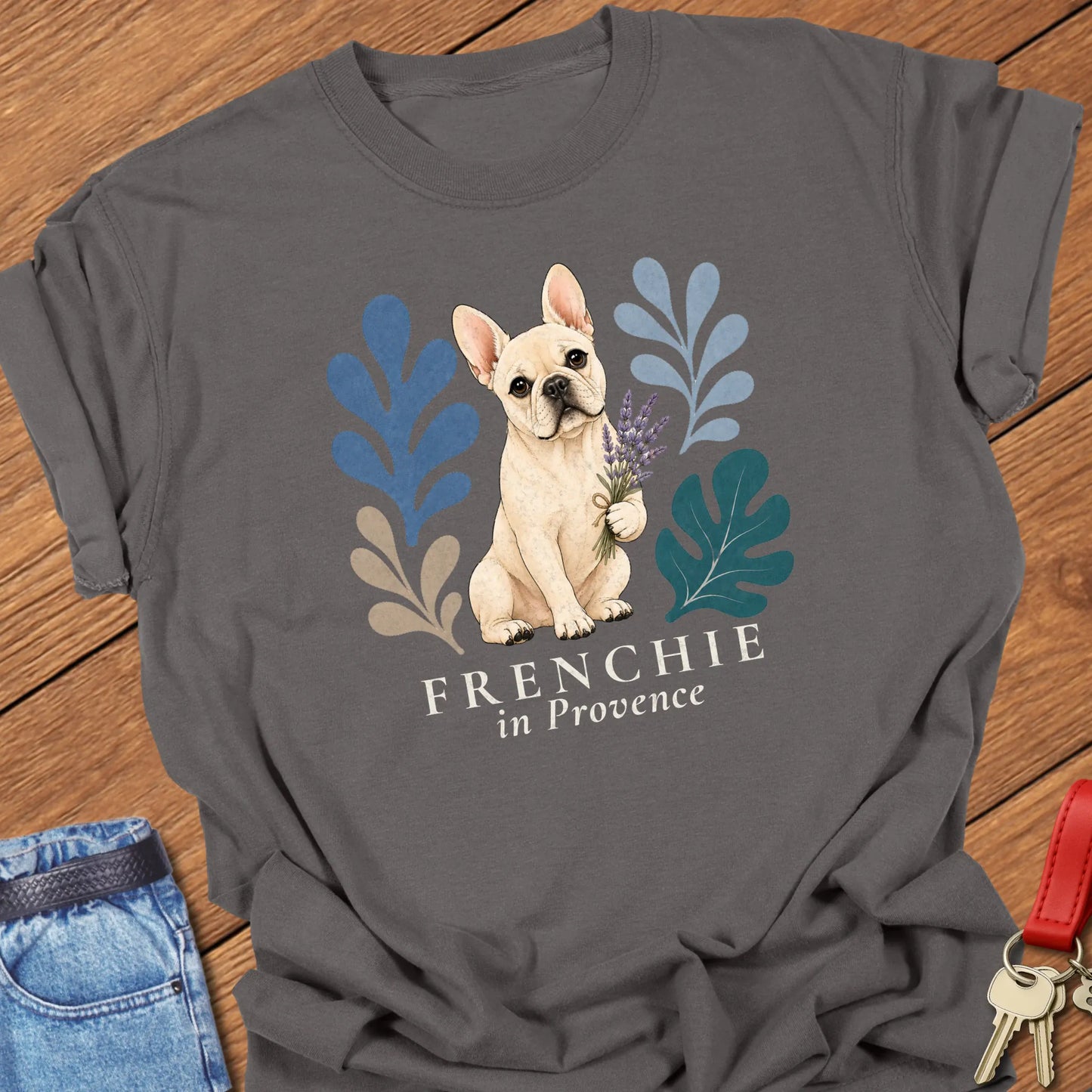 Cream French Bulldog holding a lavender bouquet surrounded by botanical artwork with the phrase "Frenchie in Provence" printed on a Comfort Colors® garment-dyed t-shirt in Pepper color.
