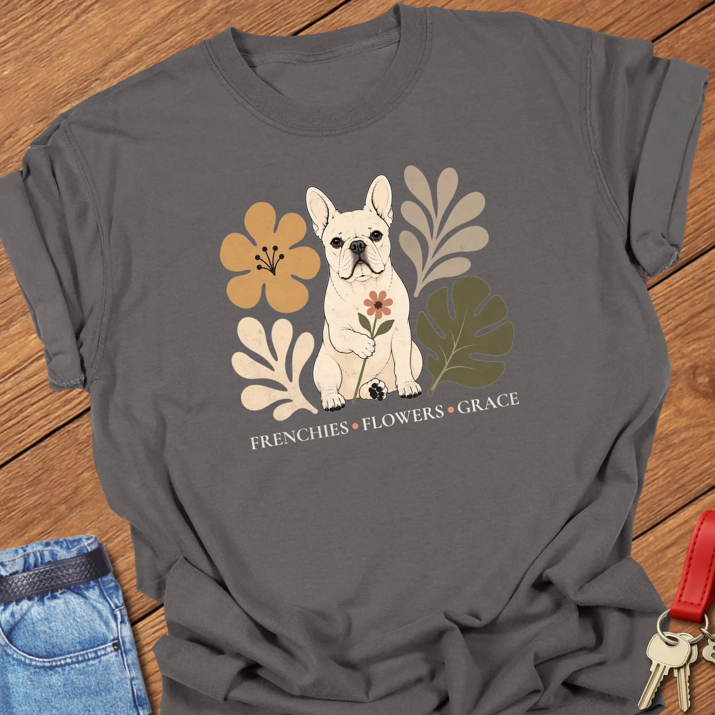 Cream French Bulldog holding a flower surrounded by modern botanical artwork with the phrase "Frenchies • Flowers • Grace" printed on a Comfort Colors® garment-dyed t-shirt in Pepper color.