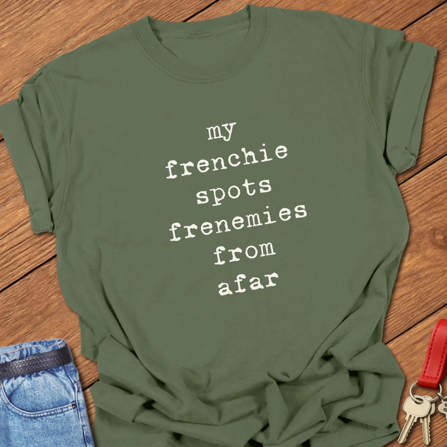 Typewriter-style typography featuring the slogan "My Frenchie Spots Frenemies From Afar" printed on a Comfort Colors® garment-dyed t-shirt in Moss color.