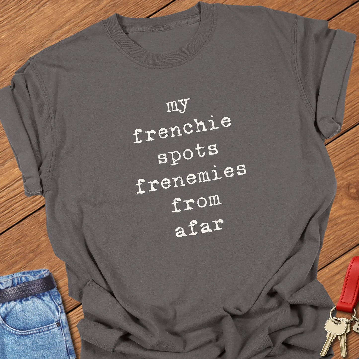 Typewriter-style typography featuring the slogan "My Frenchie Spots Frenemies From Afar" printed on a Comfort Colors® garment-dyed t-shirt in Pepper color.